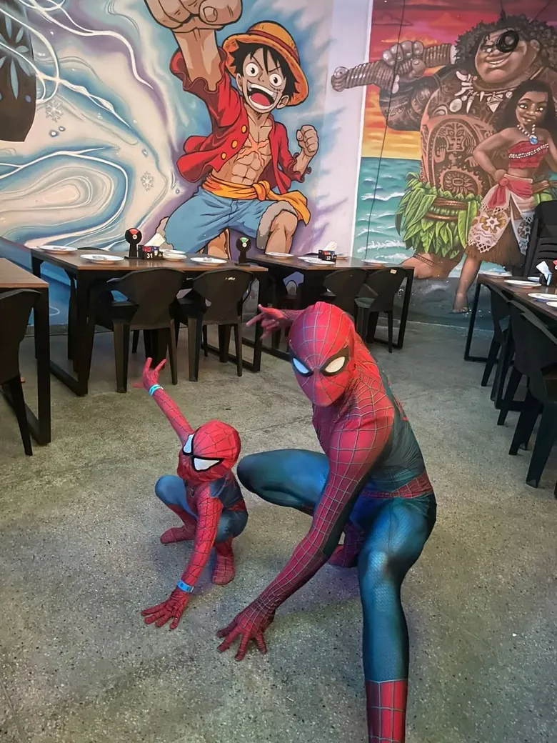 Personagens do Homem-Aranha posando no salão com mural temático ao fundo